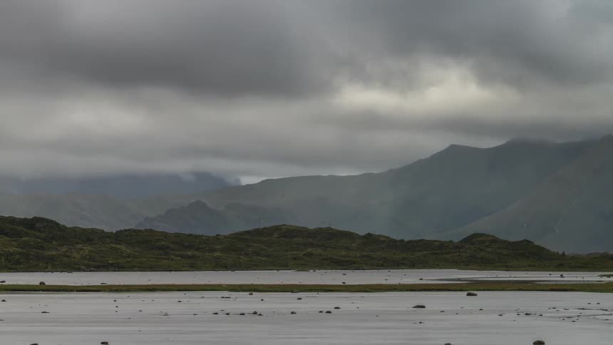 Stormy clouds passing above greenish mountains on the edge of a lake