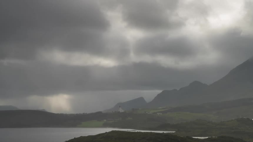 Mountainous landscape by a lake with dense clouds passing by