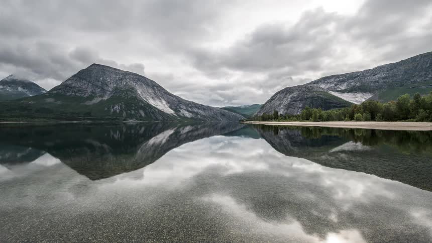 Lake reflecting surrounding snowy mountains and a cloudy sky
