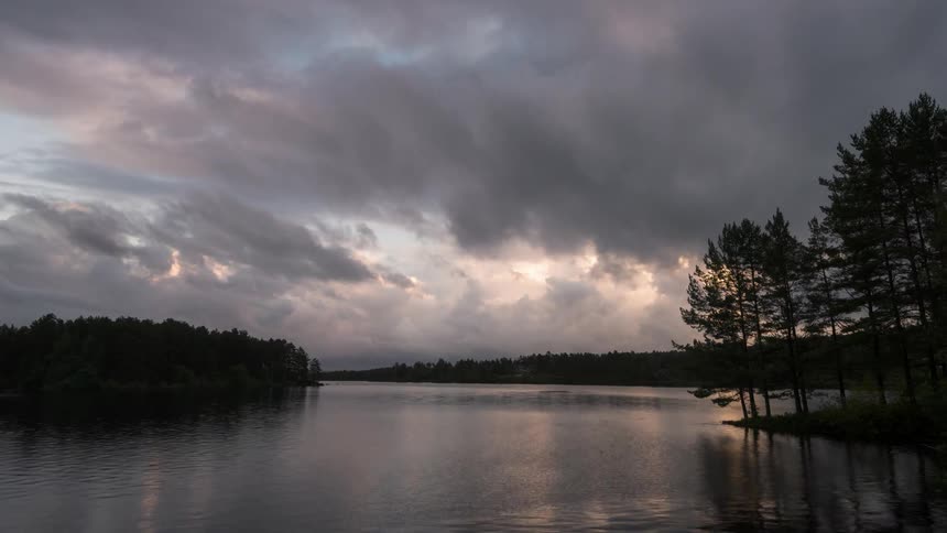 Tranquil lake with sun reflections on the water surrounded by trees under a cloudy sky