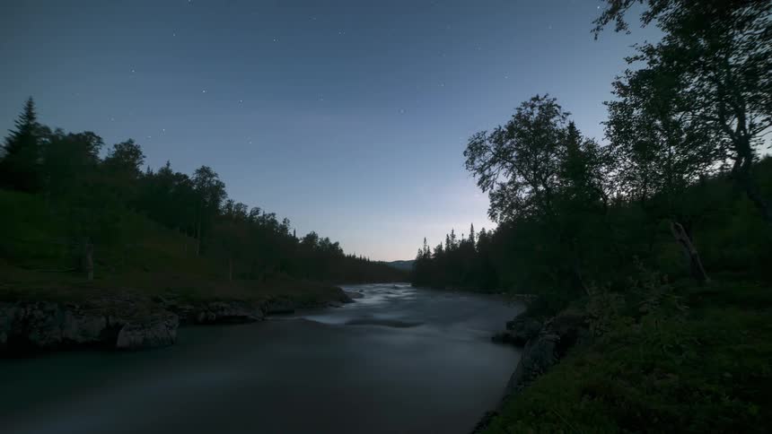 Time lapse of a river flowing through the forest as clouds and stars appear from day to night