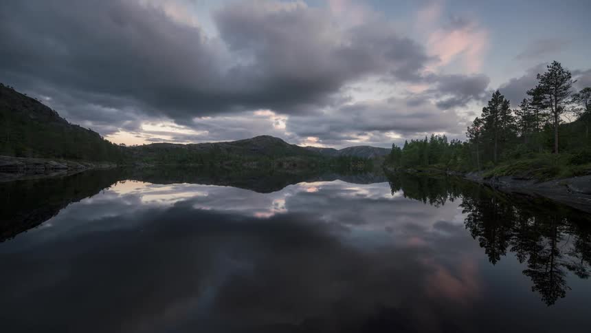 Lake reflecting surrounding mountains and trees in a cloudy sky