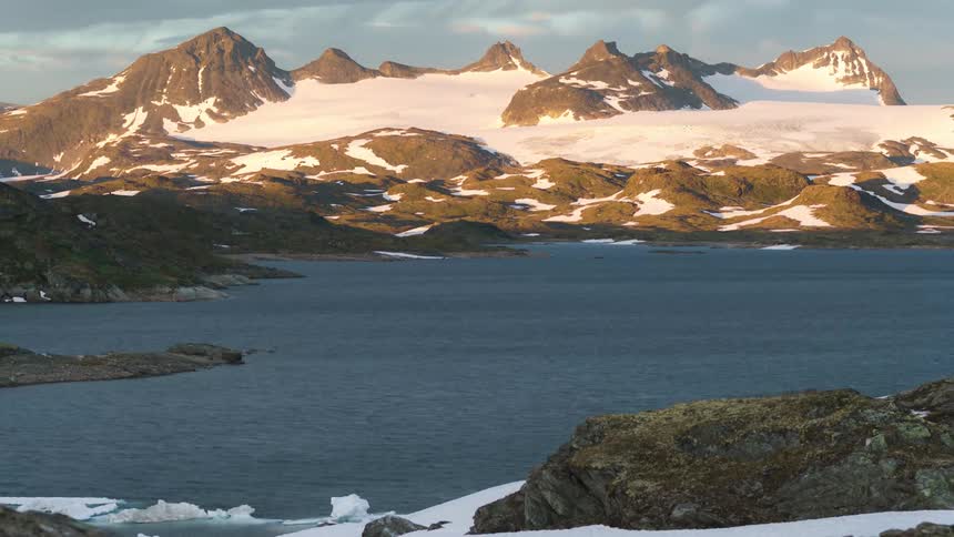 Lake surrounded by snowy mountains and in the background a partially cloudy sky that is getting dark
