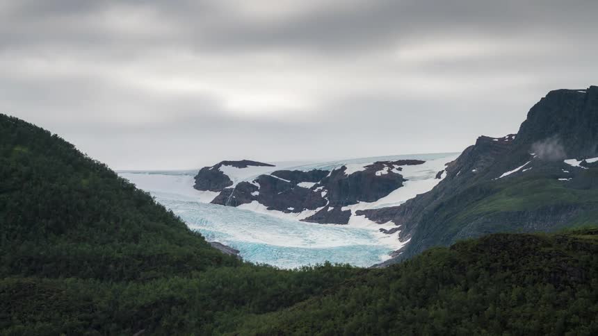 Landscape of mountains with vegetation and glaciers against a cloudy sky with dense clouds