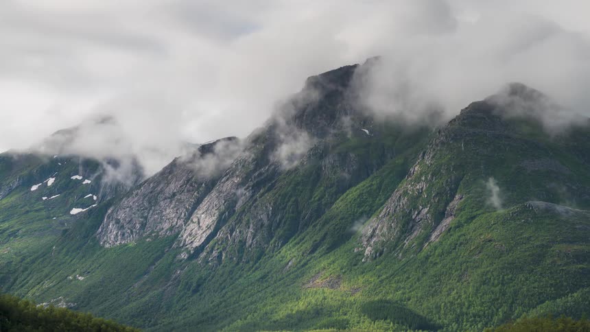 Greenish mountain range with a sea of clouds passing close to the rocky peaks