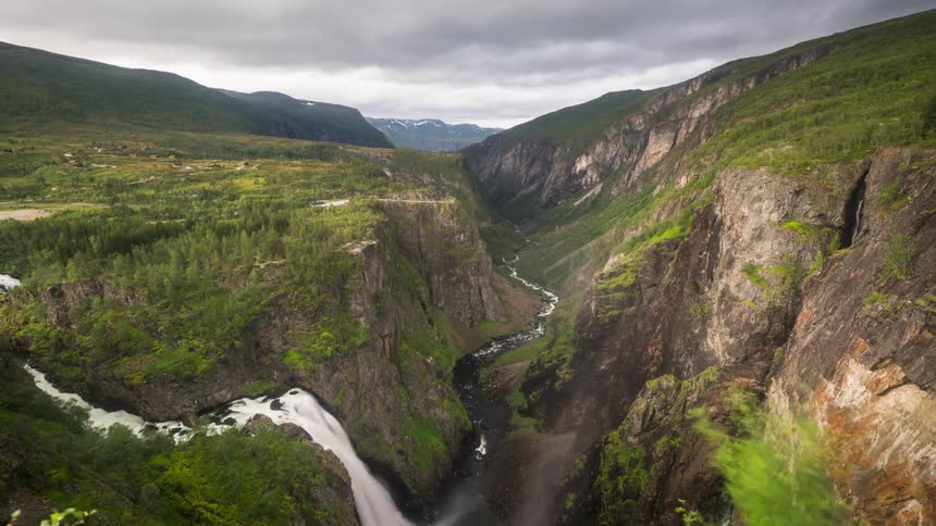 Time lapse of a waterfall plunging down a steep cliff into a river in the mountains