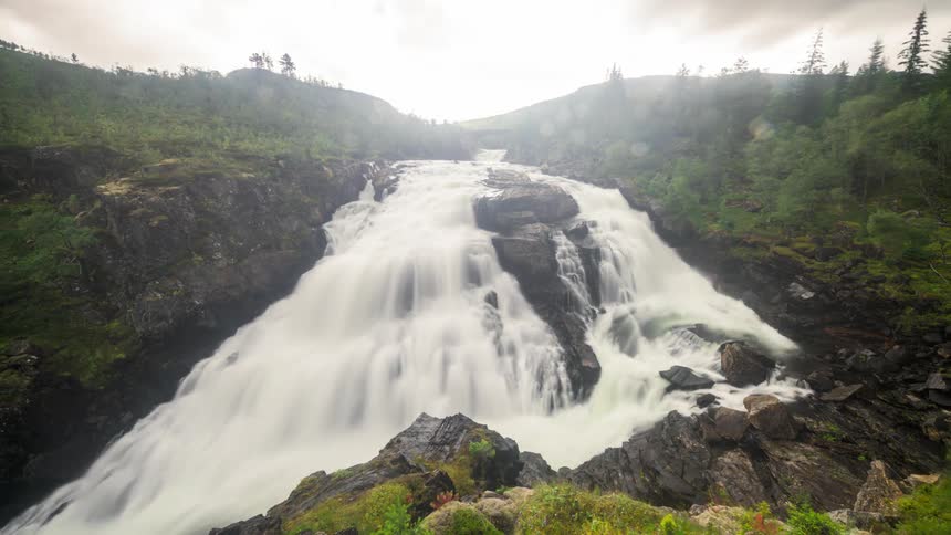 Time lapse of a river flowing down in the forest as clouds roll by