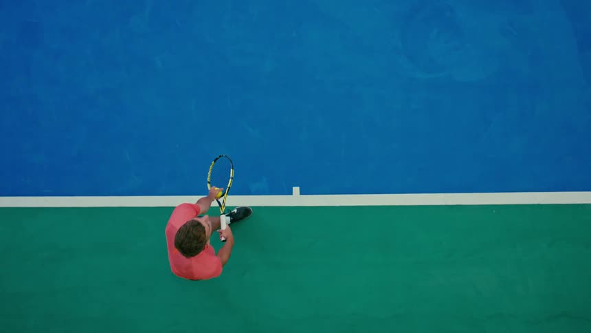Overhead view of a man serving a tennis ball across the tennis court