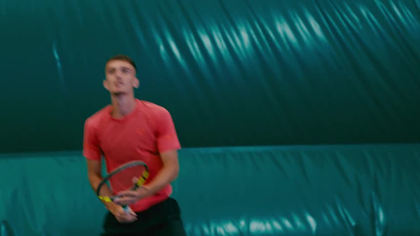 A tennis player wearing a red shirt returns a ball with his racket