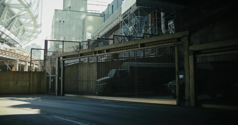 Street view with a moving car passing industrial buildings with metal structures and mesh fences