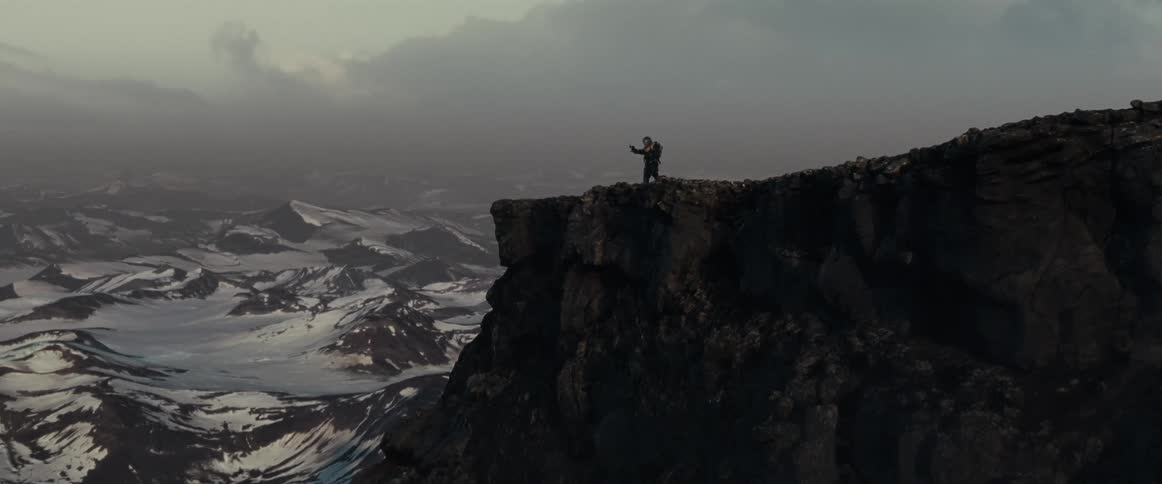 A man stands on the top of a mountain and films his surroundings on a smartphone