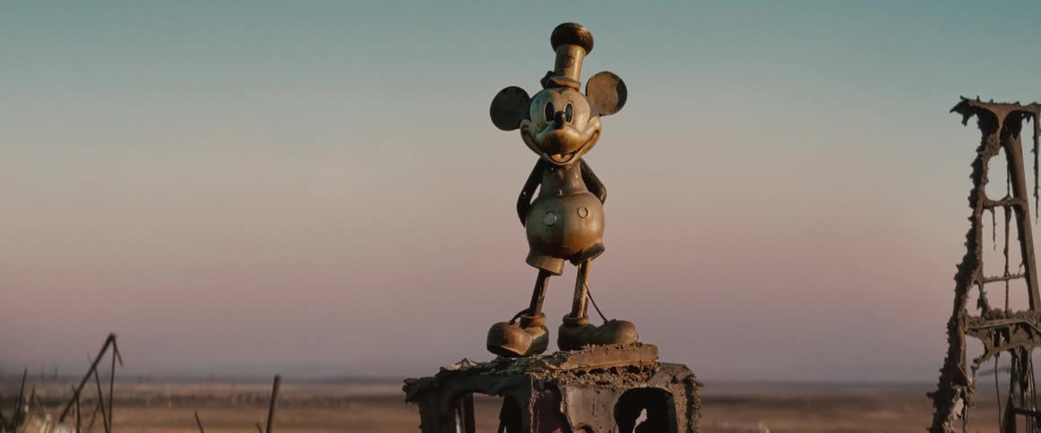 Mickey mouse statue on a rusty surface in a desolate setting with damaged structures in the background