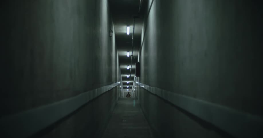 Long narrow corridor lit by fluorescent lights and a person walking in the background