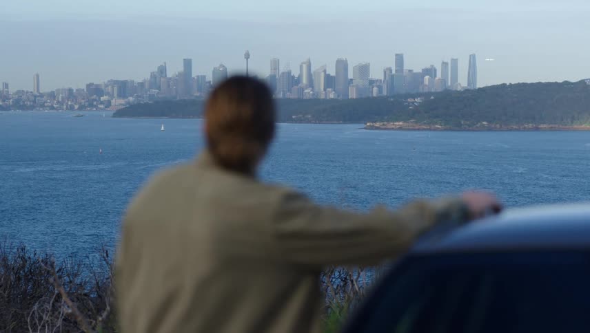 A man is standing near his parked car and looking at the skyline