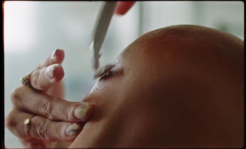 Person with tattoos and painted fingernails shaves their head