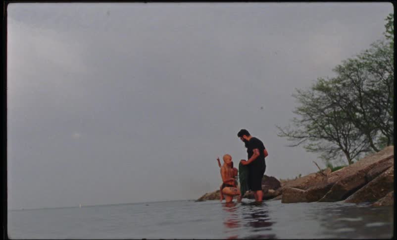 A woman wading with her child goes over to a man and hugs him