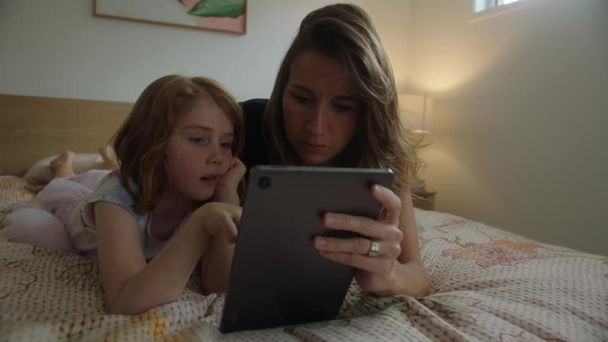 Mother lying in bed with her daughter using the tablet
