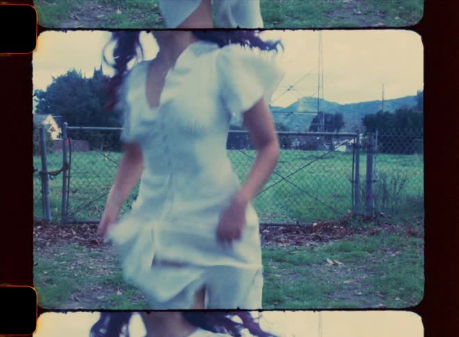 A teenage girl in a white dress is running and there is a metal fence behind her