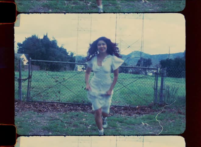 Woman in a white dress is one side of a railing in an open field running smiling