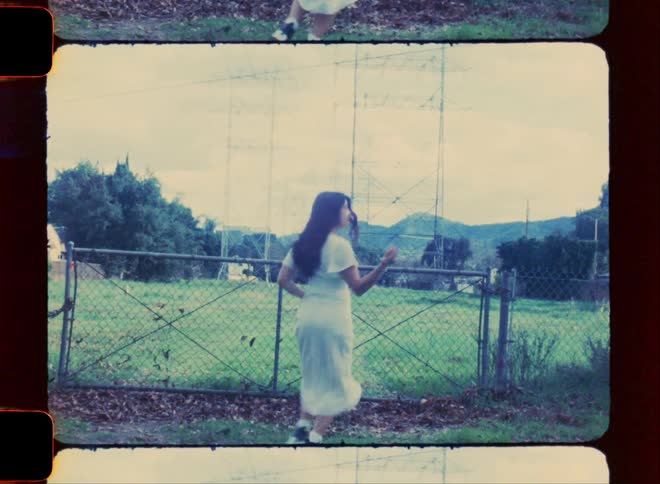 Woman in a white dress running towards a fence in an openair environment