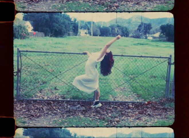 A teenage girl performs exaggerated dance moves while holding on to a chain link fence