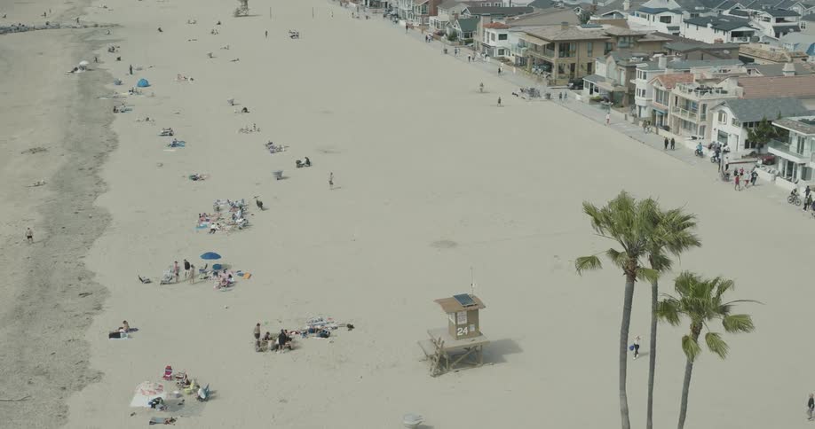 Many people walking on a beach or a boardwalk by nearby homes and buildings