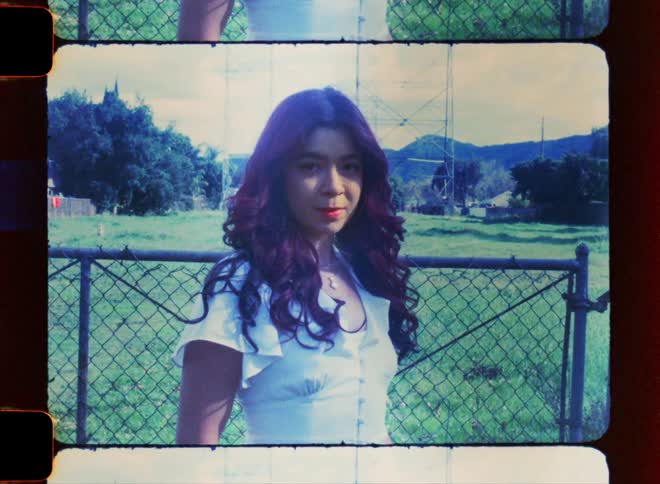 Hispanic woman with long hair posing in front of a chain link fence on a field outdoors