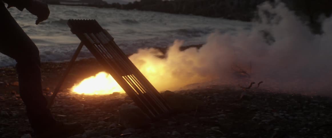 Person standing next to a fire pit by the water