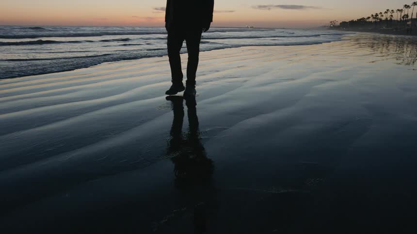 Silhouette of a man walking on the shoreline at the beach at dusk