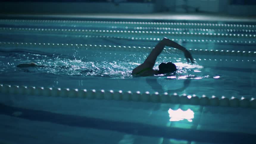 A woman swimming alone in a dimly lit pool