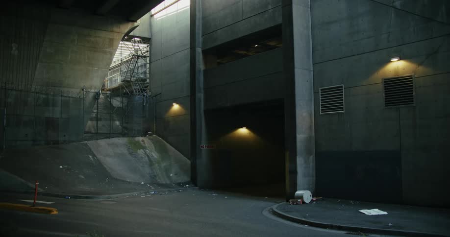 A large building has lights illuminating its exterior as a driveway leads to a garage