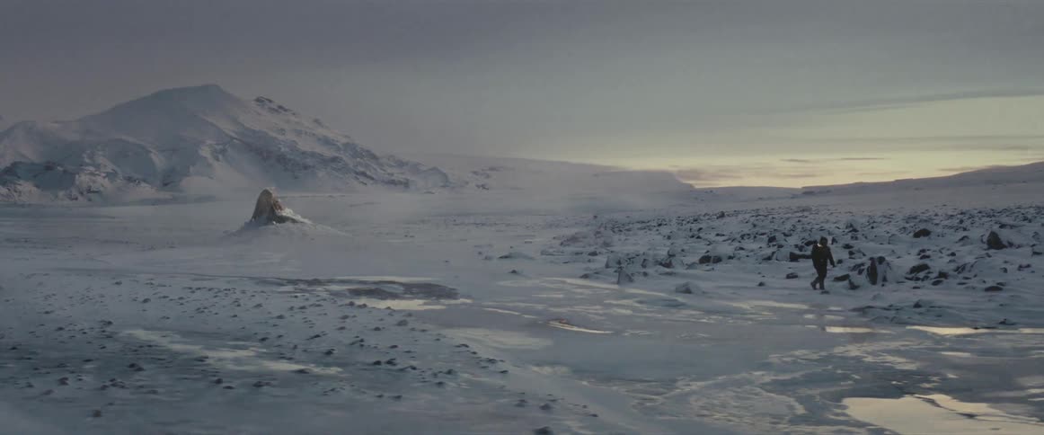 Person walking in an environment covered in snow and in the background a large alien emerging from the ground