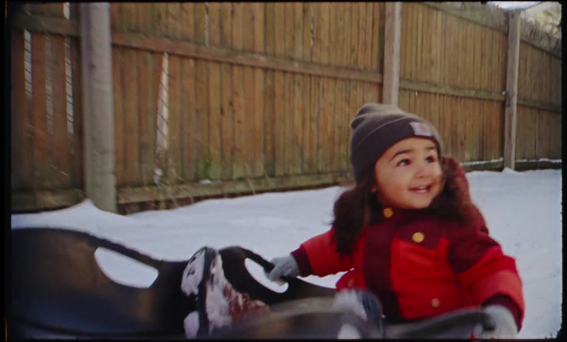 Happy child being pulled on a snow sled in the backyard