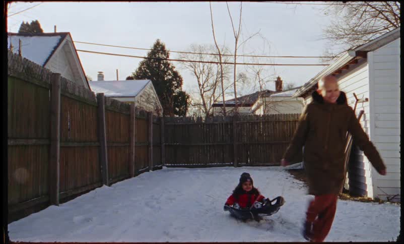 Mother pulls daughter on a sled in the snow in the backyard