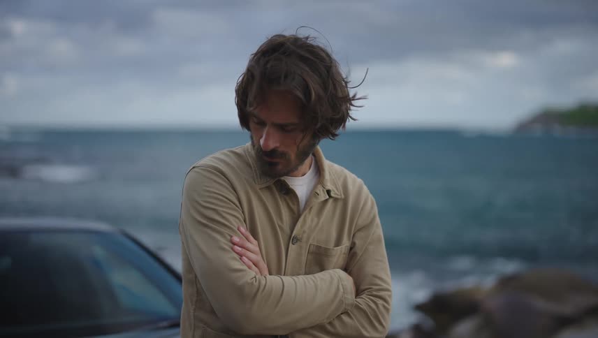 A man is standing by a parked car on the coast of a beach