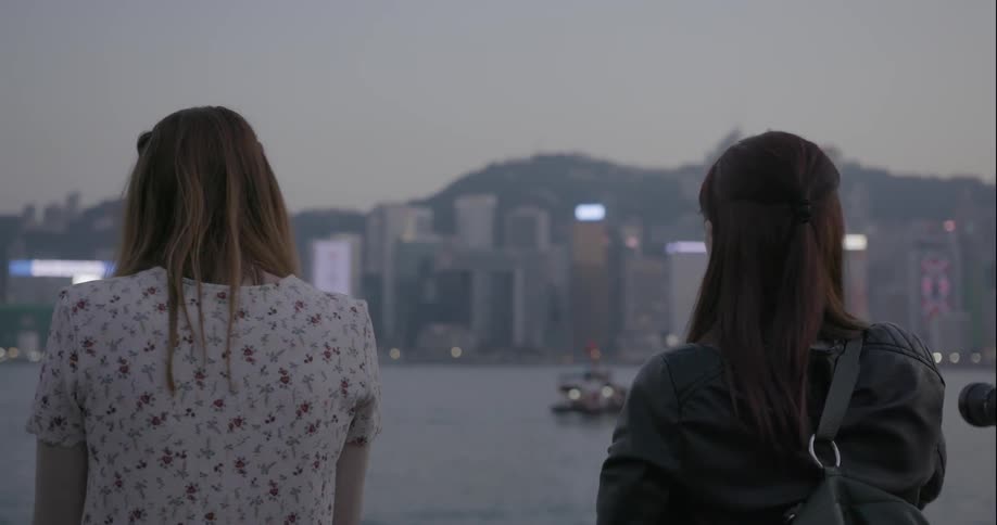 Two women taking pictures of and observing city skyline