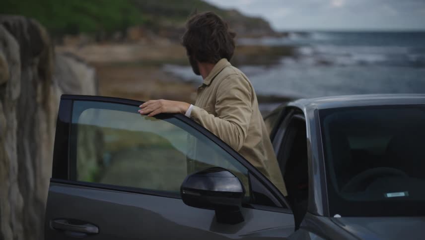 Man getting out of the car and closing the door in a setting on the rocky coast by the sea