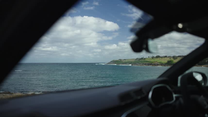A coastal area and grassy plain seen through a car window