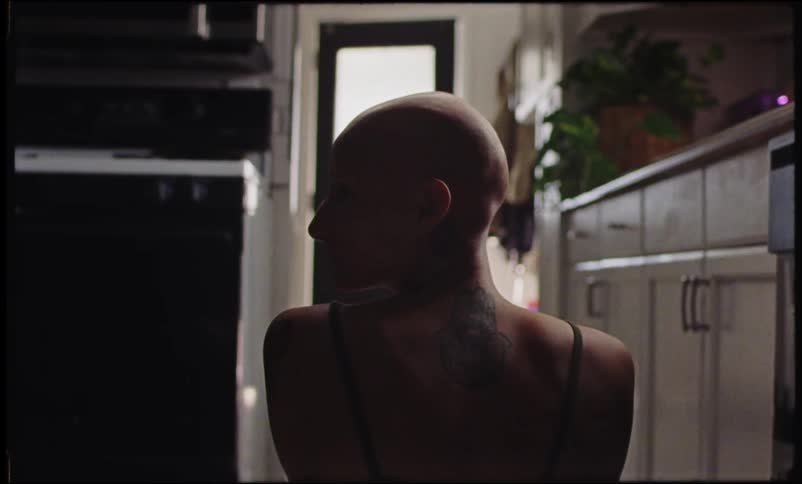 A girl with long hair and a bald tattooed woman in the kitchen at home