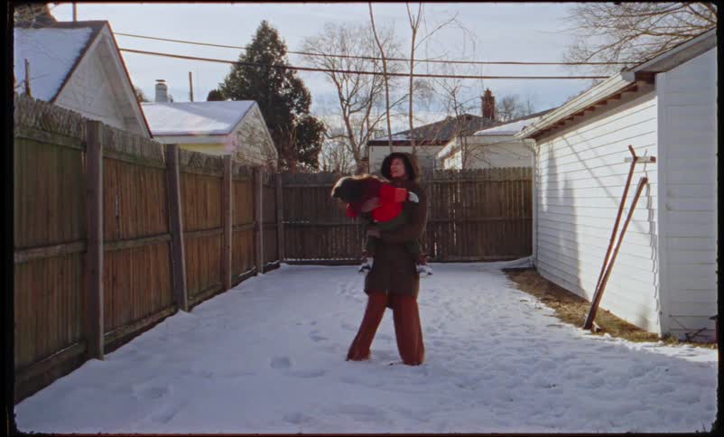 Mother holding and twirling her child while playing in the snow in the backyard