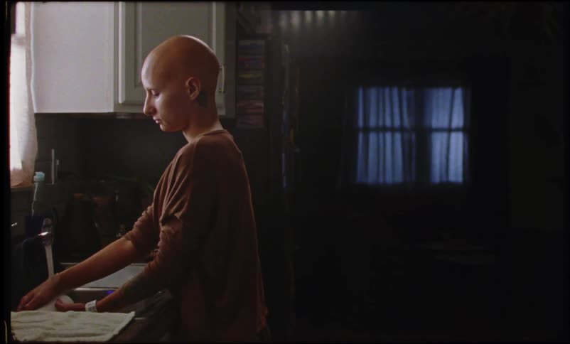 Bald woman washing dishes in the sink as moonlight shines through the window