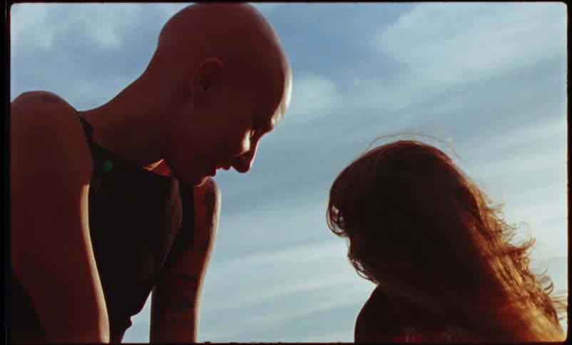 Girl with long hair plays with a bald tattooed woman outdoors