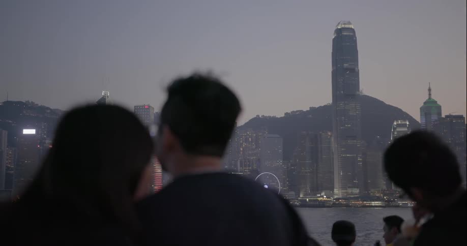 A couple stands with a crowd of people looking at a city skyline at dusk