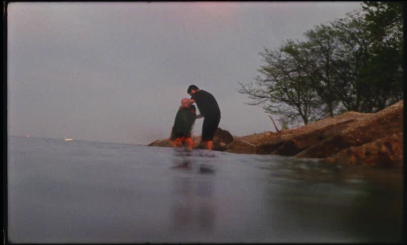 Man hugging a woman who is holding a child while they are at a lake