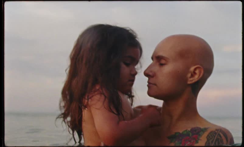 A bald mother holding her child and bouncing in the ocean