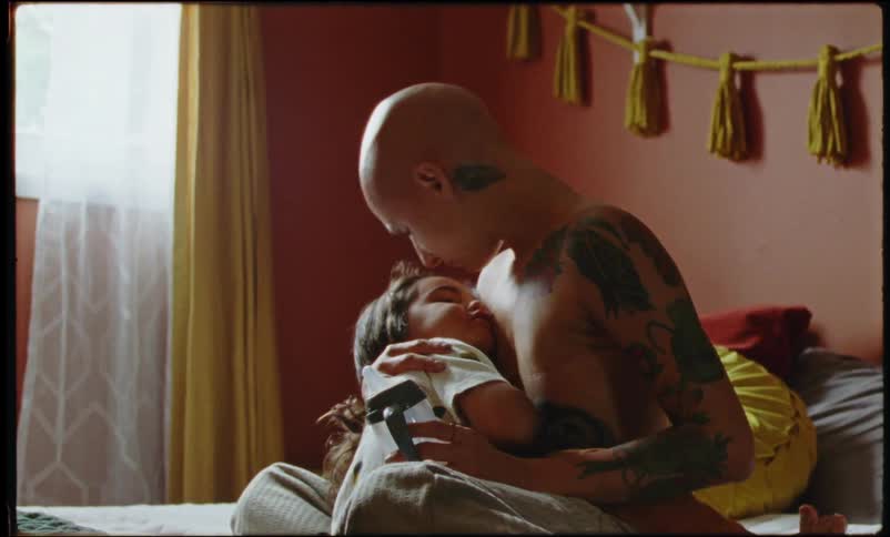 Mother sitting on the bed with her daughter on her lap and putting a kiss on her face