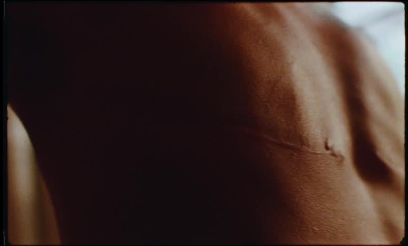 A tattooed person takes bandages out revealing scars over his chest
