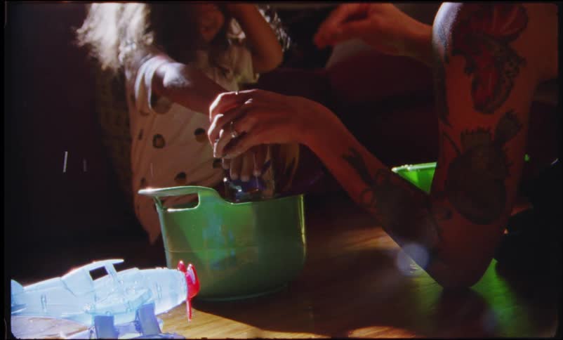Mother and daughter play with water from a jar over a green bowl in the living room