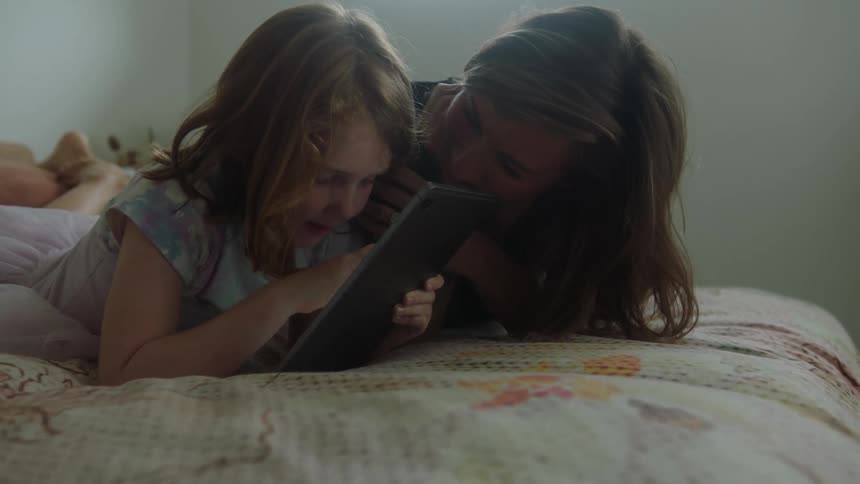 Mother and daughter play together with a tablet in the bedroom