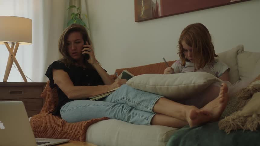 Mother lying on the sofa next to her daughter while talking on the phone